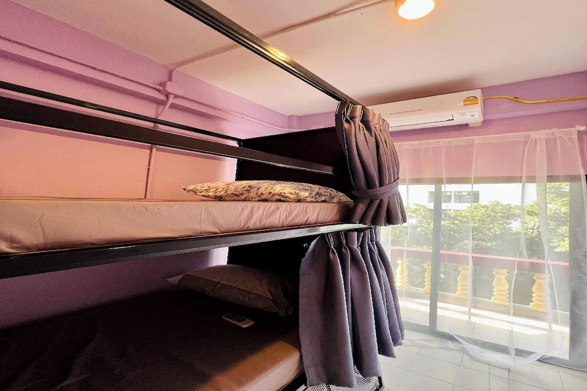 A bunk bed room with a window, curtains, and an air conditioning unit.