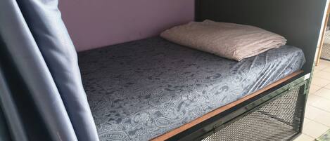 Una cama individual con una colcha estampada y una almohada, un mueble de almacenamiento metálico debajo y una pared morada.