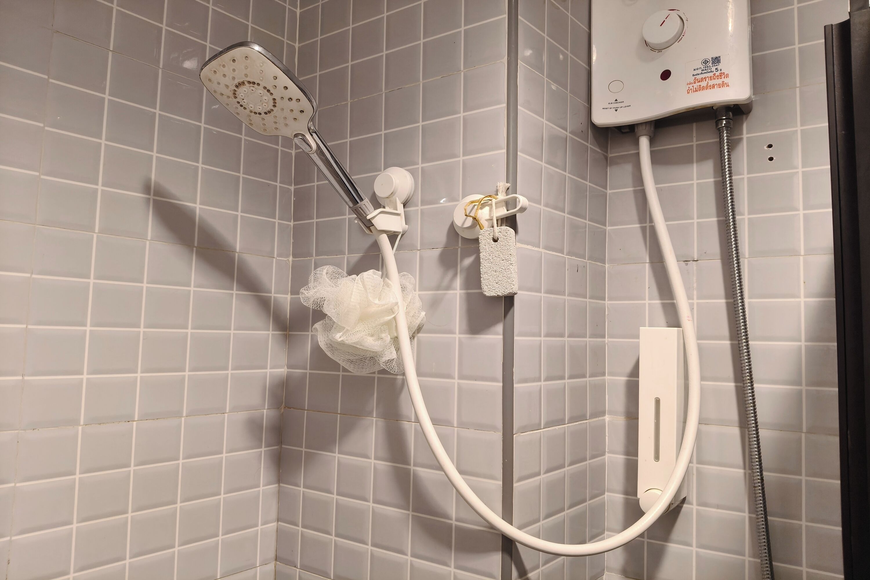 A shower with a handheld showerhead and a wall-mounted control panel.
