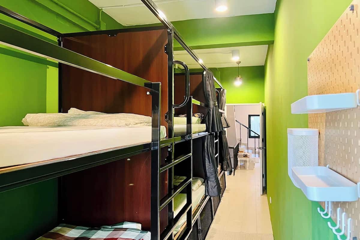 A bunk bed room with green walls and a white ceiling. There are hooks on the wall and a small shelf.