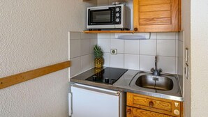 A compact kitchen with wooden cabinets, a microwave, a sink, and a small refrigerator. - Plein Océan by Interhome (Carnac)