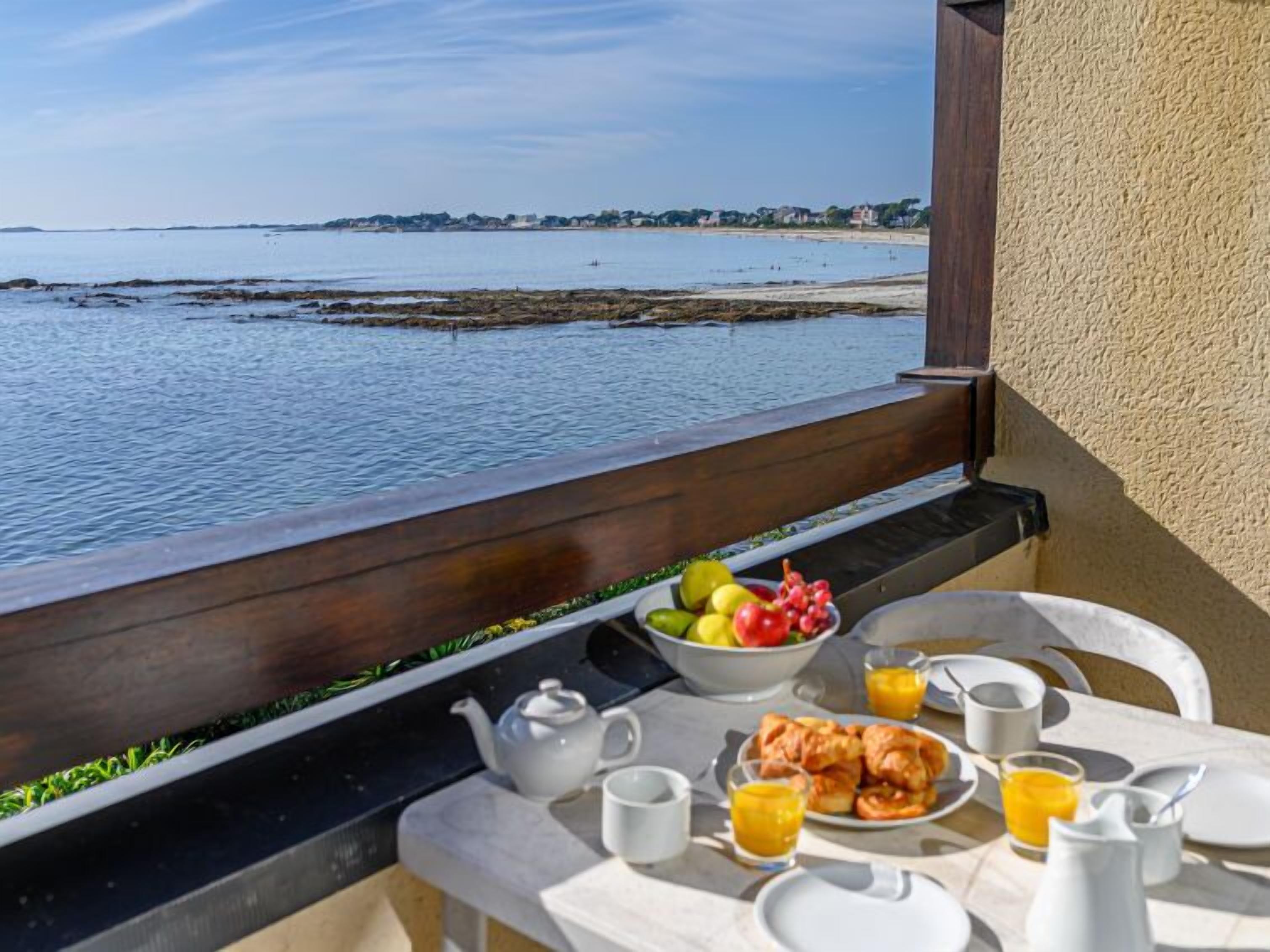 A balcony table with breakfast items, a teapot, and a view of the sea.