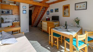 A cozy room with wooden beams, a kitchenette, a dining area with a table and chairs, and a staircase leading to another level. - Plein Océan by Interhome (Carnac)