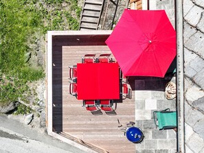 A top-down view of a deck with a red umbrella, a table with chairs, and a bicycle.