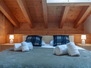 A wooden cabin bedroom with a high ceiling, two bedside lamps, a bed with white and blue striped pillows, and rolled white towels on the bed.