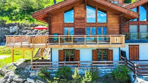 A two-story wooden cabin with a balcony, stone foundation, and a view of a mountainous landscape. - Sneachta by Interhome (Nendaz)