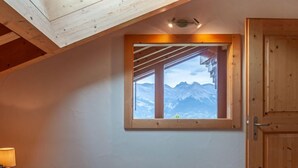A bedroom with a wooden ceiling, a window with a mountain view, a bed with a rolled towel, and a wooden door. - Sneachta by Interhome (Nendaz)