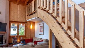 A wooden staircase leading to an upper level, a living room with a sofa, a fireplace, and a bookshelf. - Sneachta by Interhome (Nendaz)