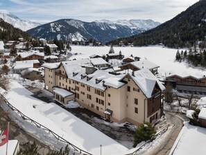 Eine verschneite Bergstadt mit einem großen Hotel, das aus mehreren Gebäuden besteht, einer Seilbahn und Blick auf schneebedeckte Berge.