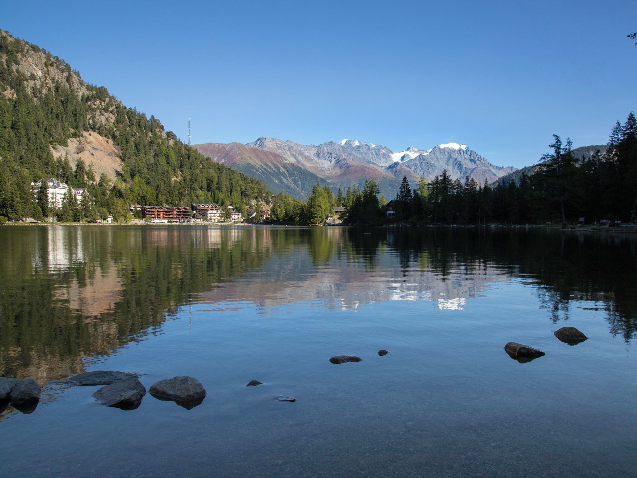 A calm lake with clear reflections of surrounding mountains and trees.