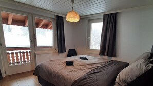 Ein Schlafzimmer mit Bett, Stuhl, Pendelleuchte und Fenstern mit Vorhängen.