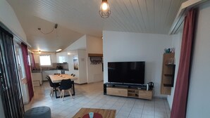 Ein modernes Wohnzimmer mit Fernseher, Couchtisch aus Holz und Poufs.