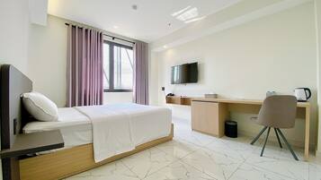 Quarto de hotel com cama, escrivaninha, cadeira, televisão e janela com cortinas.