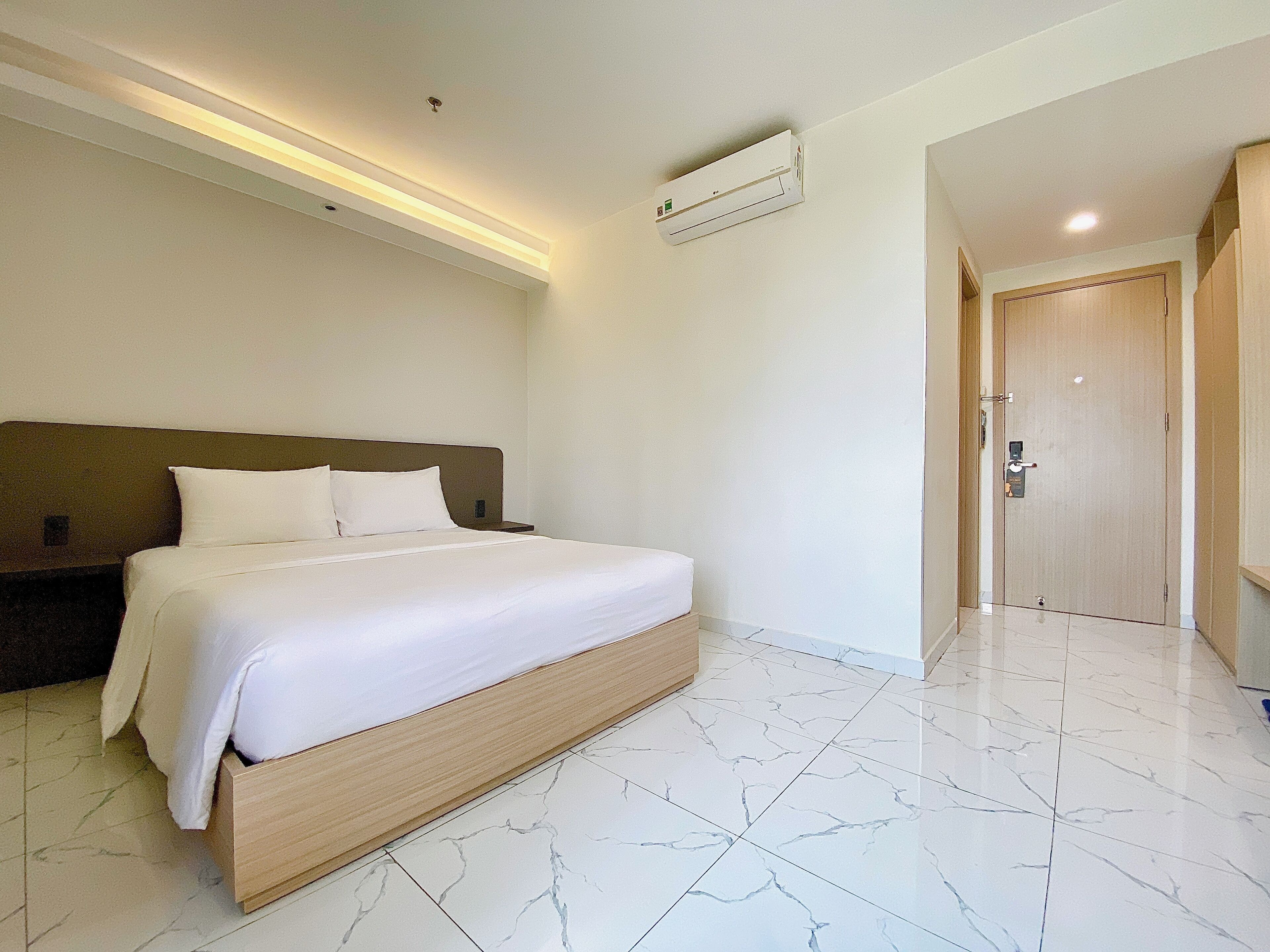 Una habitación de hotel con una cama, una mesita de noche, un cabecero de madera, un aire acondicionado blanco y una puerta.