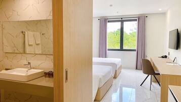 Quarto de hotel com banheiro de mármore, duas camas, uma escrivaninha e uma televisão.