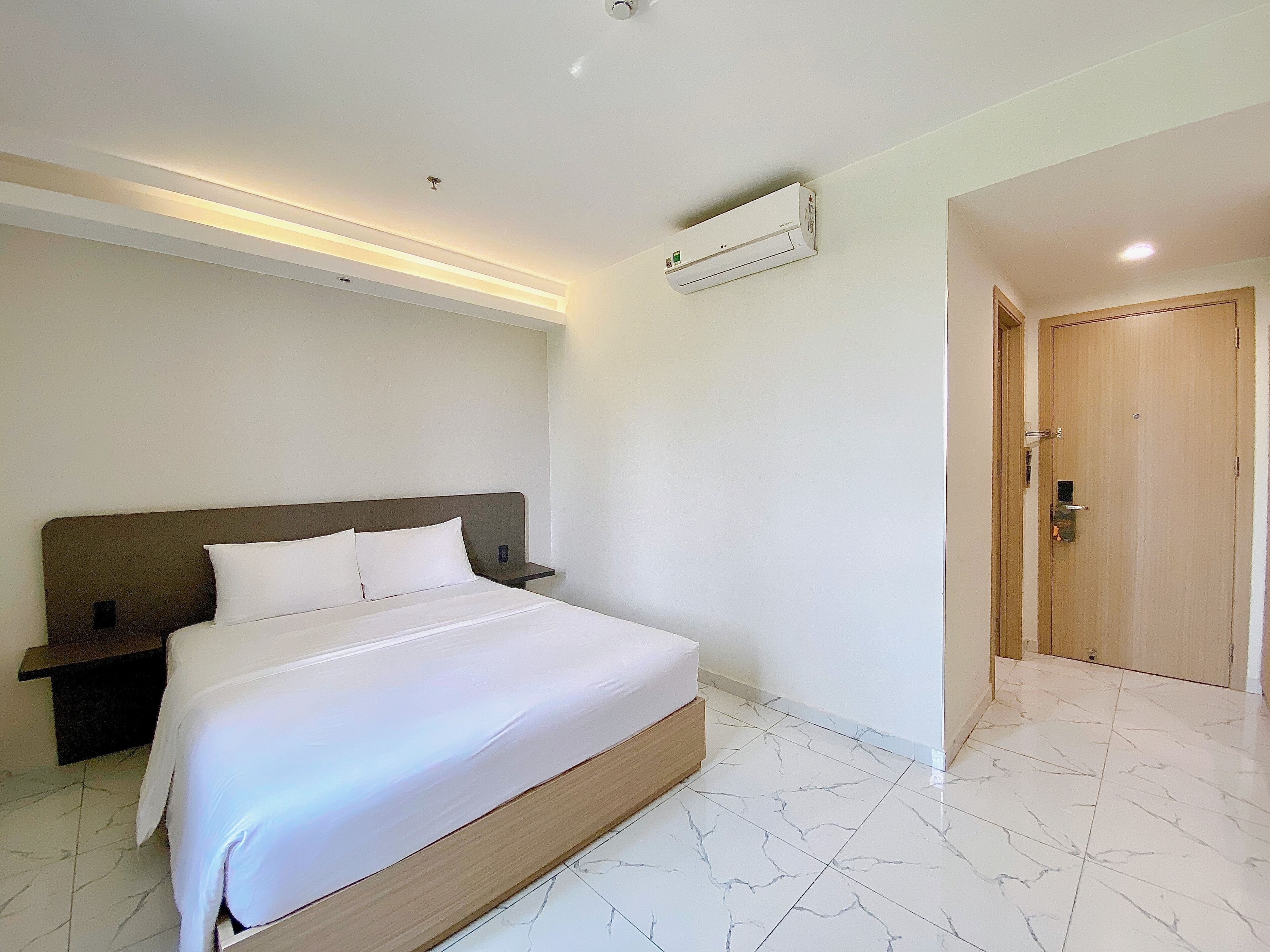 Een moderne hotelkamer met een groot bed, een nachtkastje, een wandairconditioner en een houten deur.