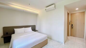 A modern hotel room with a large bed, a nightstand, a wall-mounted air conditioner, and a wooden door.