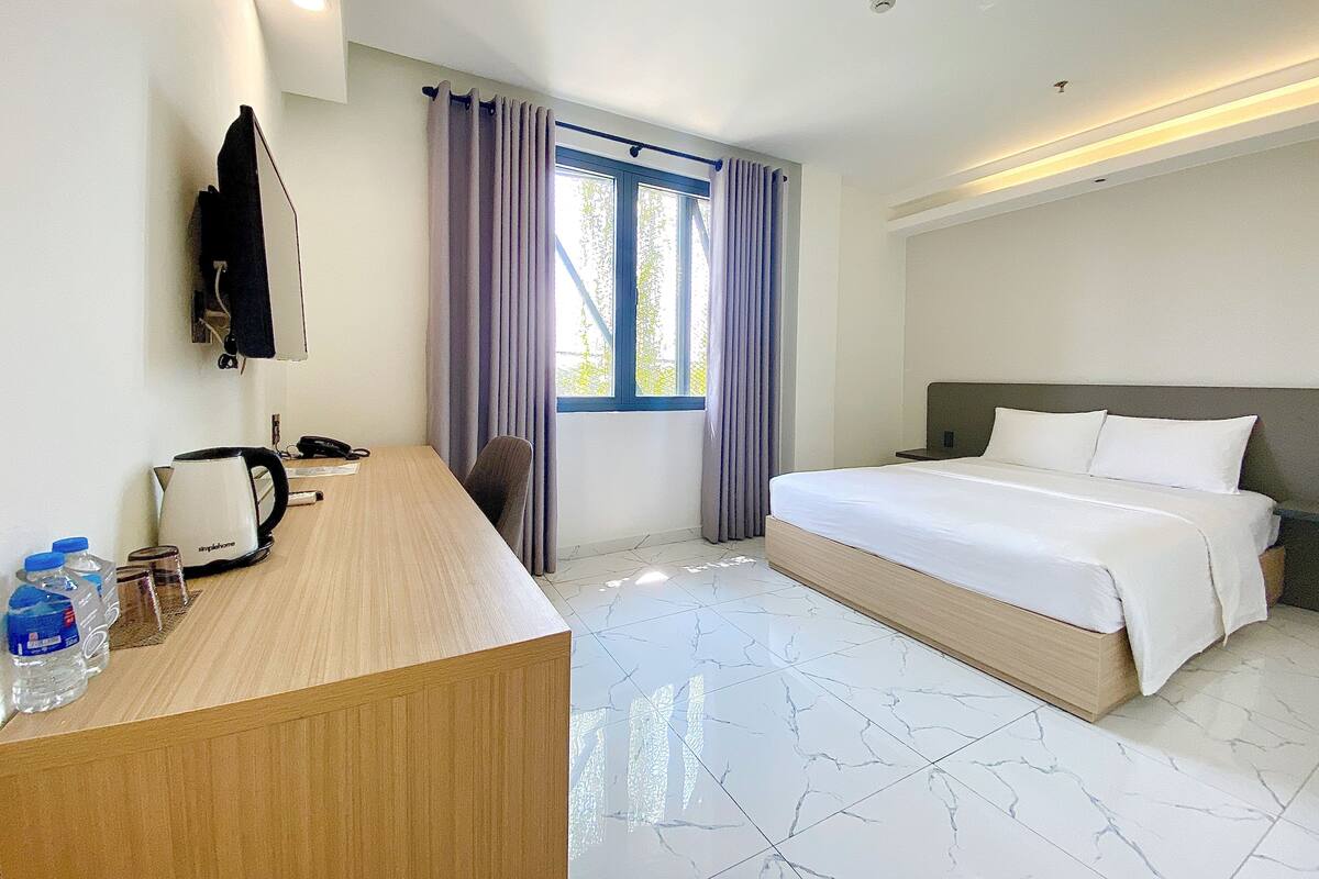 Habitación de hotel con cama, escritorio con teléfono y ventana con cortinas.
