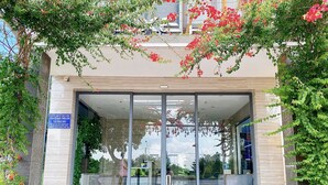A modern building entrance with glass doors, a signboard, and a paved area with a bench. - The Luxe Hotel - Chau Doc (Chau Doc)