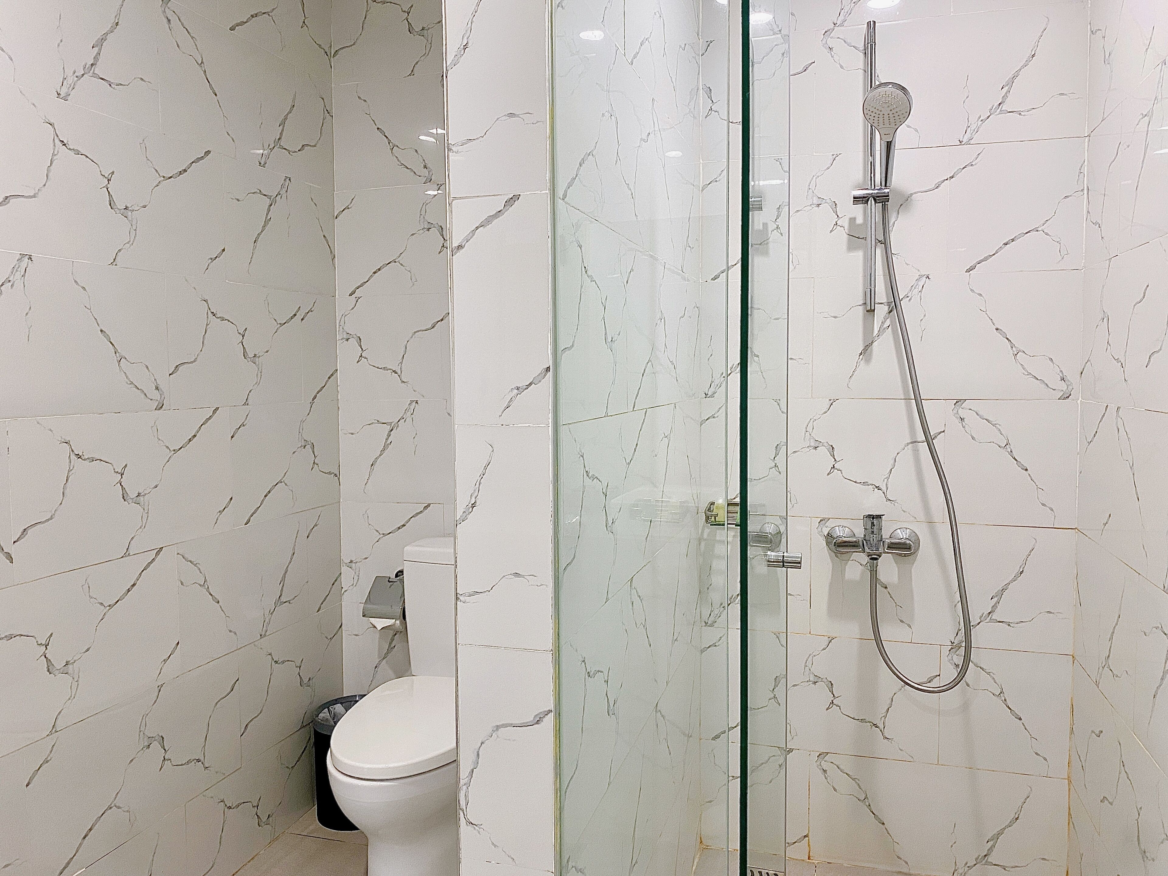 Un baño con ducha envuelta en vidrio, inodoro y paredes con diseño de mármol.