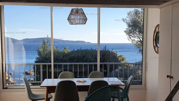A dining area with a table and chairs, a view of the sea and hills, and a hanging light fixture. - Large mezzanine studio with sea view, parking and AC near the Calanque de la Cron (Cavalaire-sur-Mer)