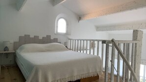 A bedroom with a wooden bed, a small window, and a white railing. - Large mezzanine studio with sea view, parking and AC near the Calanque de la Cron (Cavalaire-sur-Mer)