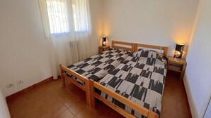 Une chambre à coucher avec un lit en bois, deux lampes de chevet, une fenêtre avec des rideaux légers et un radiateur.