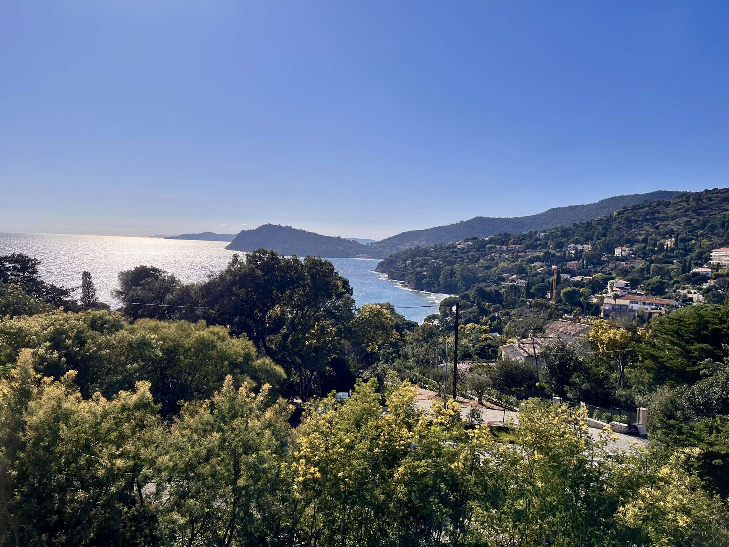 Un paysage côtier offrant une vue sur la mer, des collines et quelques bâtiments dispersés.