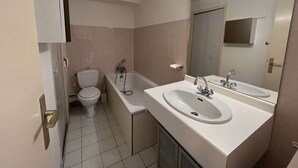Une salle de bain équipée de toilettes, d’une baignoire et d’un lavabo double, avec un miroir au-dessus.