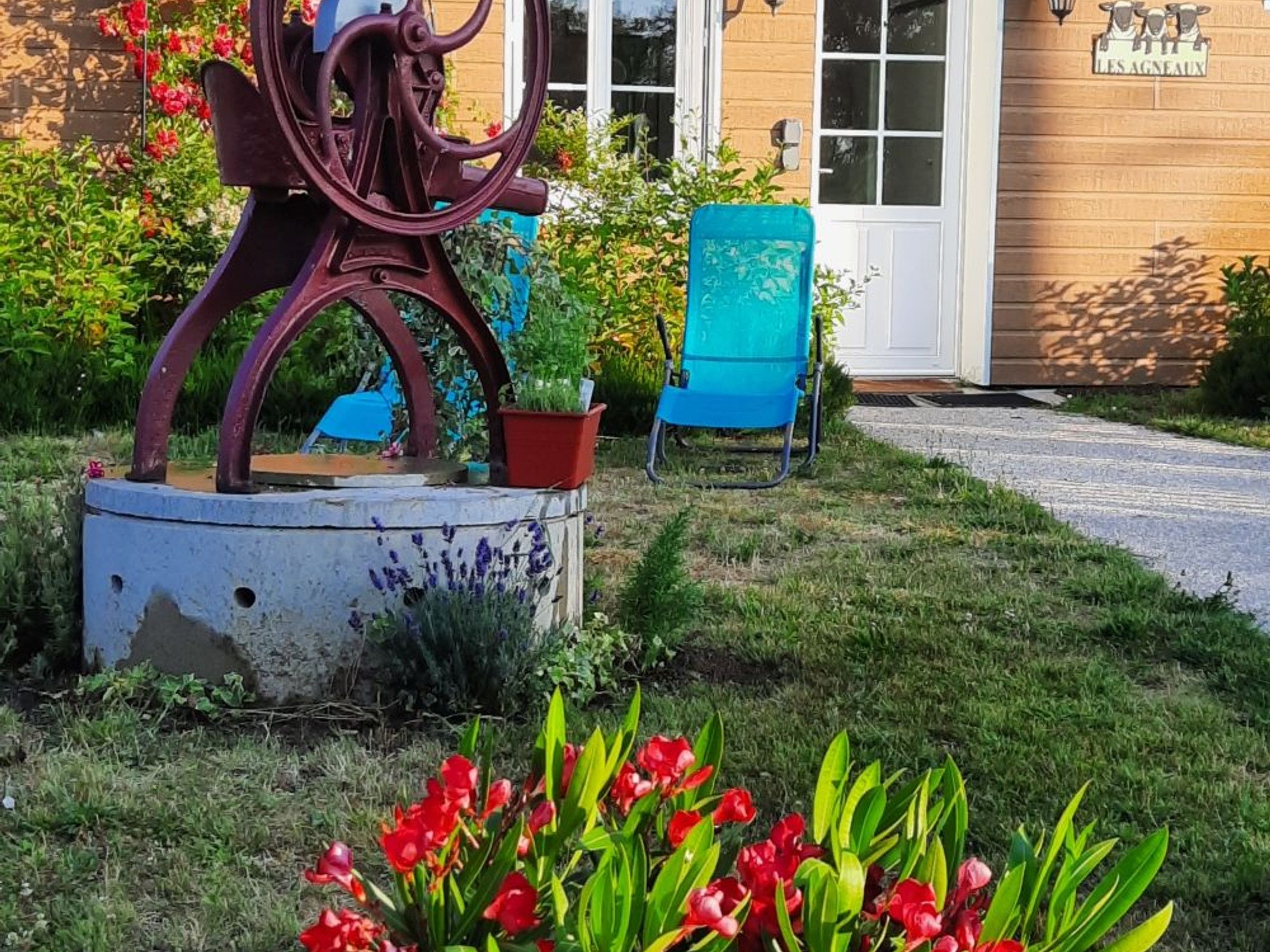 Un jardin agrémenté d’une sculpture en métal, d’une chaise bleue et de fleurs rouges.
