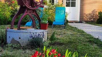 A garden with a metal sculpture, a blue chair, and red flowers.