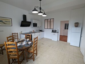 A kitchen with white cabinets, a dining table with chairs, a black ceiling light, and a refrigerator.