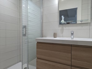 A modern bathroom with a glass shower enclosure, a wooden vanity with a mirror, and a white countertop.