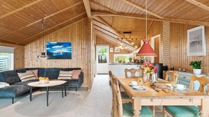 L’intérieur chaleureux d’un chalet avec un plafond en bois, un canapé, une table à manger avec des chaises et un coin cuisine.