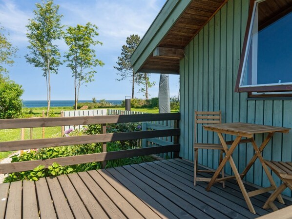 Une terrasse en bois avec une table et des chaises, donnant sur une pelouse et la mer.