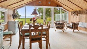Un coin repas en bois, avec une table et des chaises, une lampe suspendue et une vue sur l’extérieur.