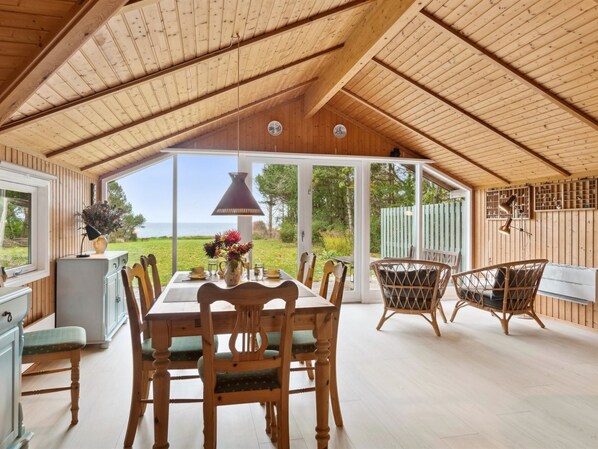A wooden dining area with a table and chairs, a hanging lamp, and a view of the outdoors.