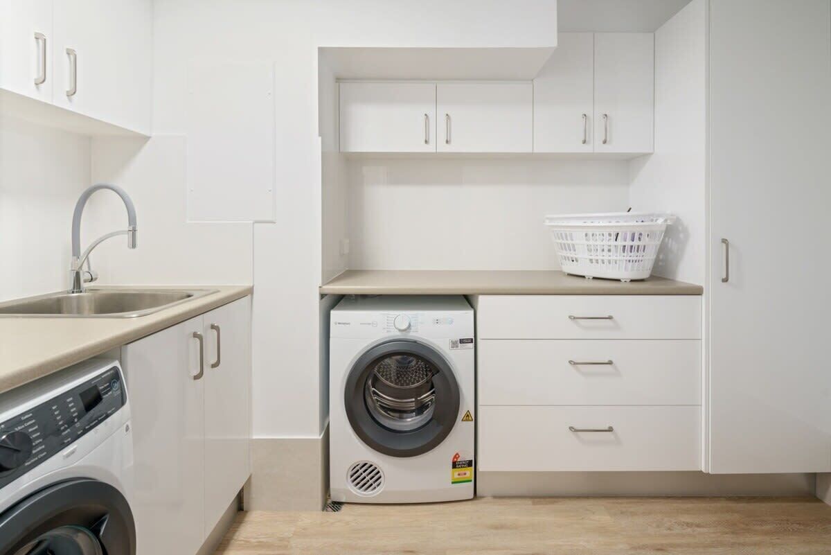A compact laundry room with a washing machine, a sink, and a drying rack.