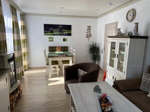 Een woonkamer met een bank, een eettafel met stoelen, een kast met glazen deuren en een klok aan de muur.