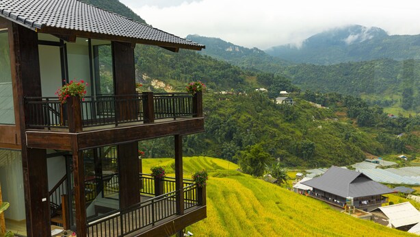 Un edificio de dos pisos con un balcón que da a un paisaje verde exuberante y montañas distantes.