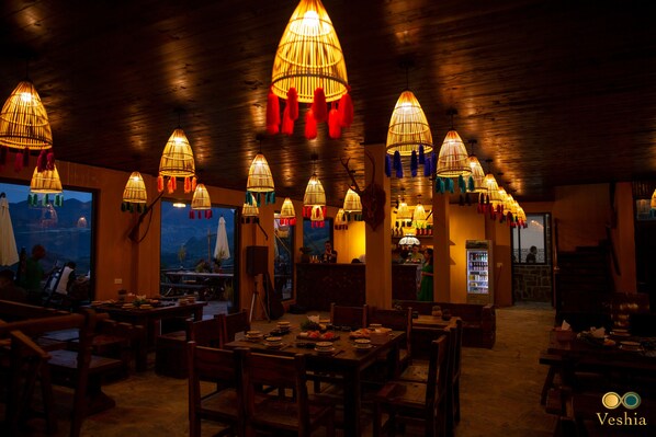 A restaurant with multiple dining tables and chairs, warm lighting, and a view of the outdoors.