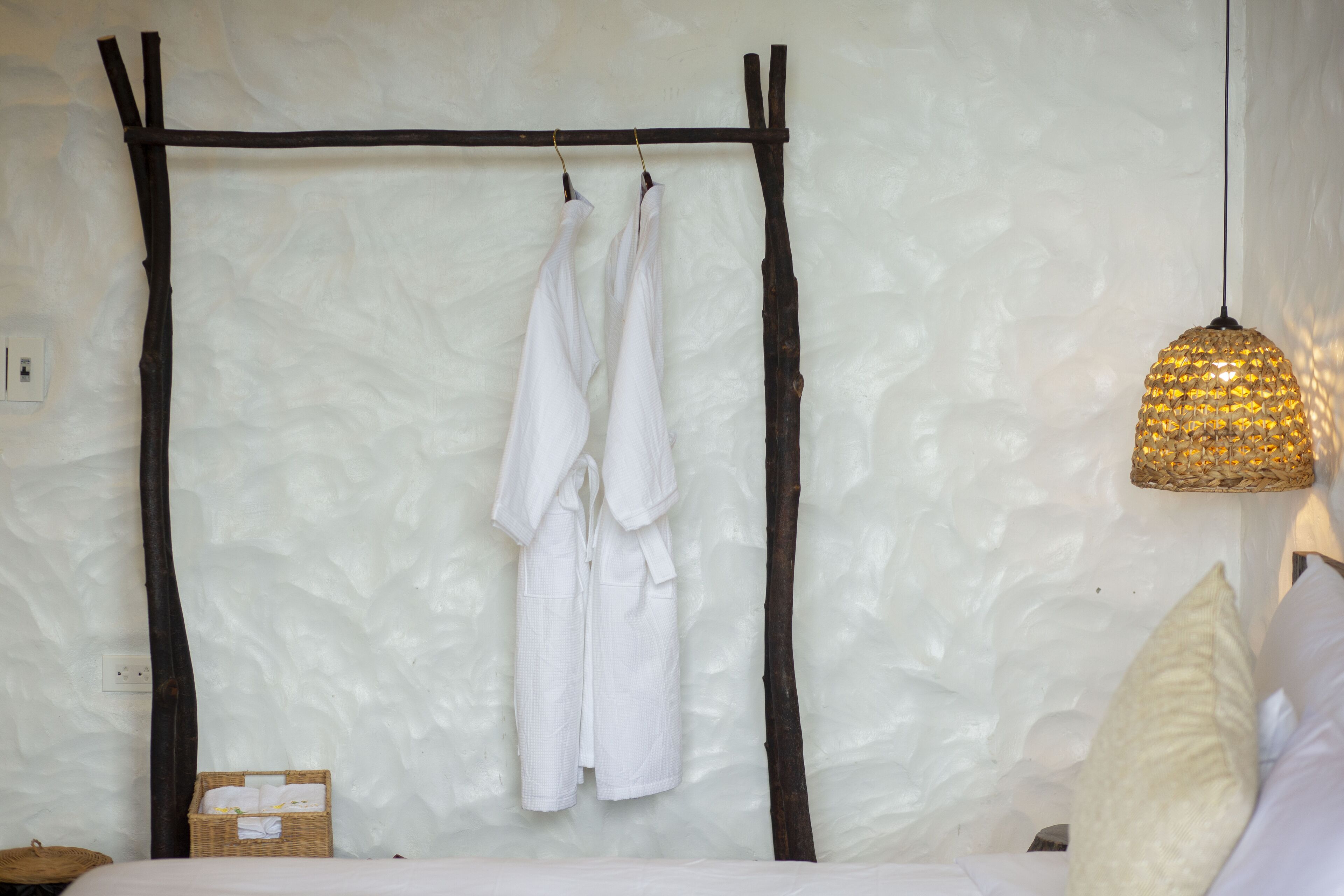 Ein Schlafzimmer mit einem Bett, einem Kleiderhaken, einem Korbwäscheschrank und einer strukturierten Wand.