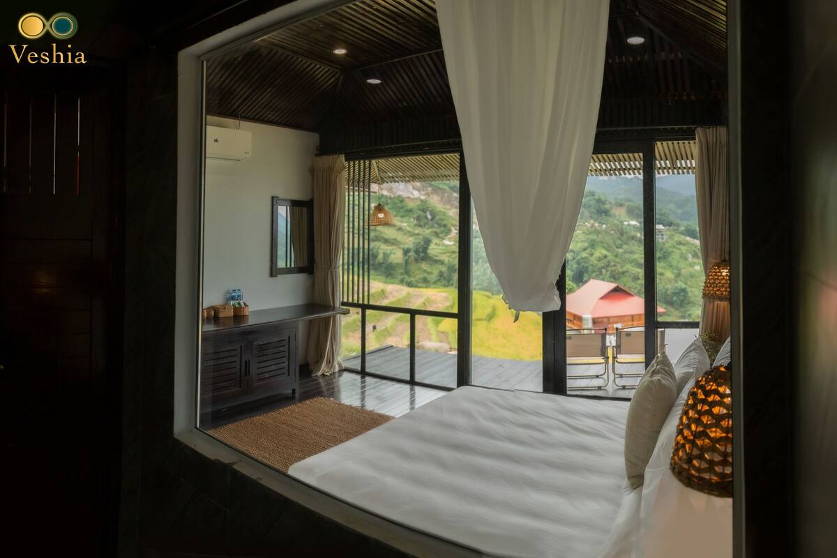 A bedroom with a large bed, a nightstand, a mirror, and a window with curtains.