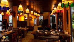 Un restaurante con mesas y sillas de madera, lámparas colgantes y una zona de bar.