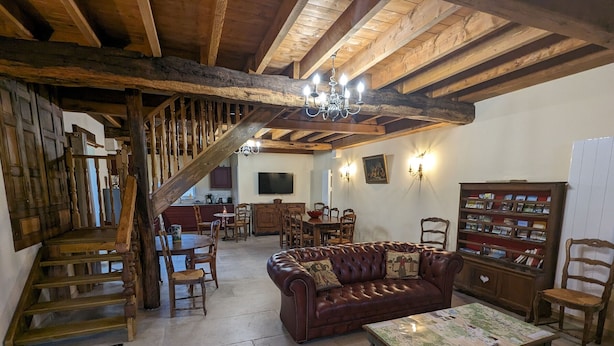 Un intérieur rustique avec des poutres apparentes, un canapé en cuir, une table à manger et une bibliothèque.