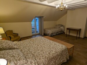 A bedroom with a large bed, a chair, a small table, and a window with curtains.