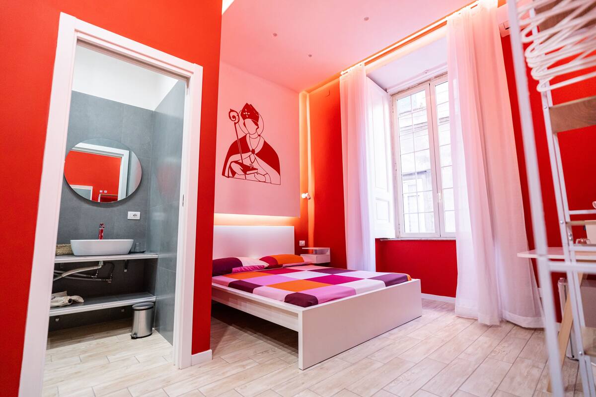Ein modernes Schlafzimmer mit einem Bett, ein Badezimmer mit einem Waschbecken und ein Fenster mit Vorhängen.