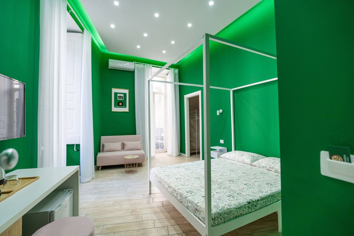 Ein modernes Schlafzimmer mit einem Himmelbett, einem Schreibtisch mit Stuhl, einer Couch und einem großen Fenster.