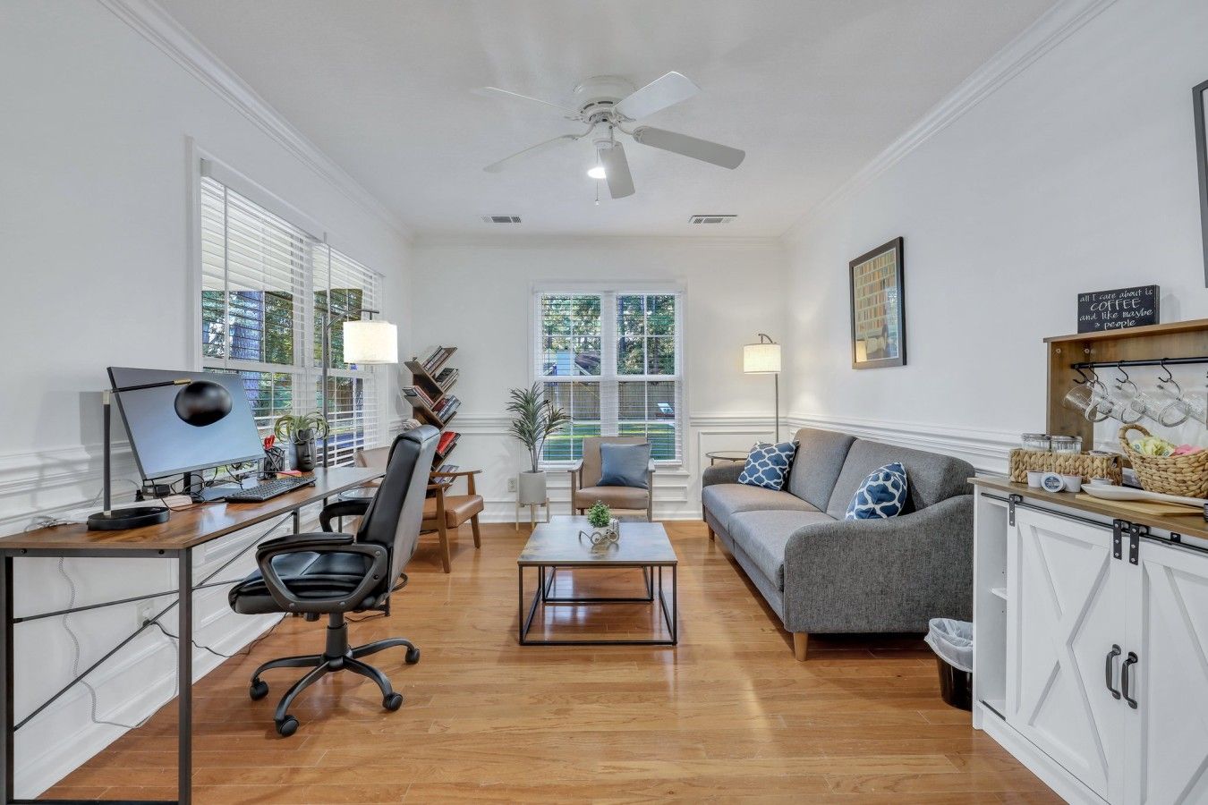 A spacious living area with a desk, office chair, sofa, and a coffee station.