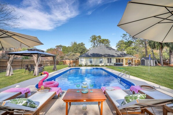 A backyard with a swimming pool, lounge chairs, and umbrellas.